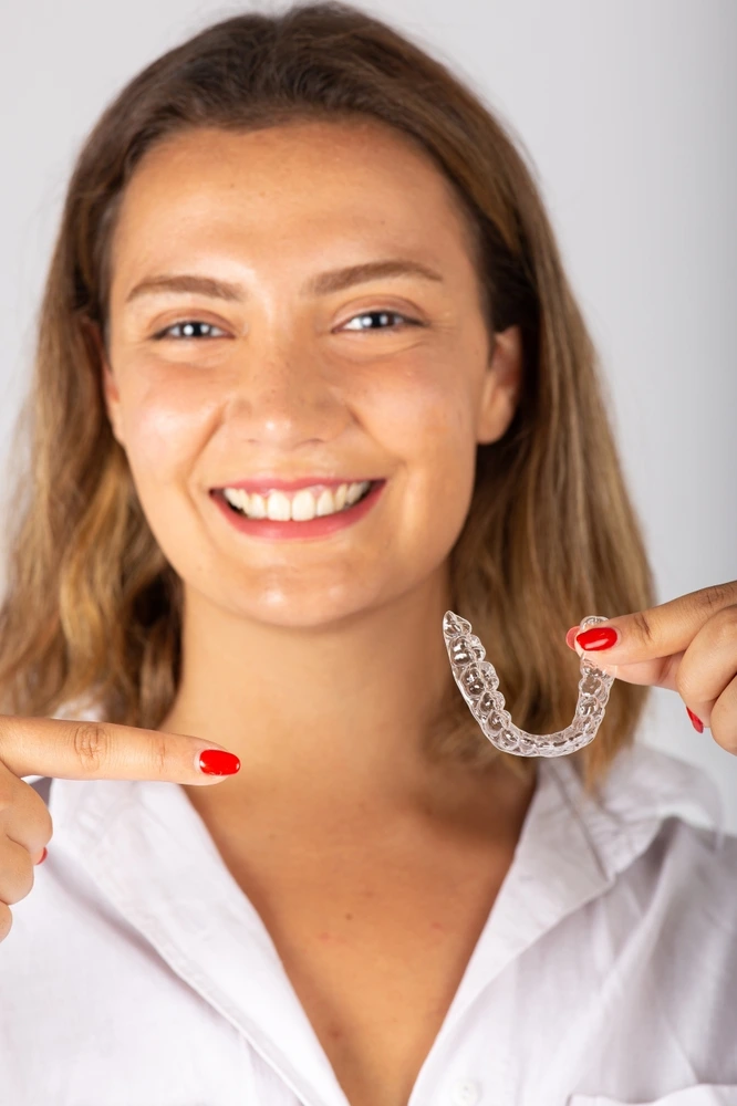 Smiling woman points to a clear aligner, excited about teeth straightening at Clearly Dental Riverwood.